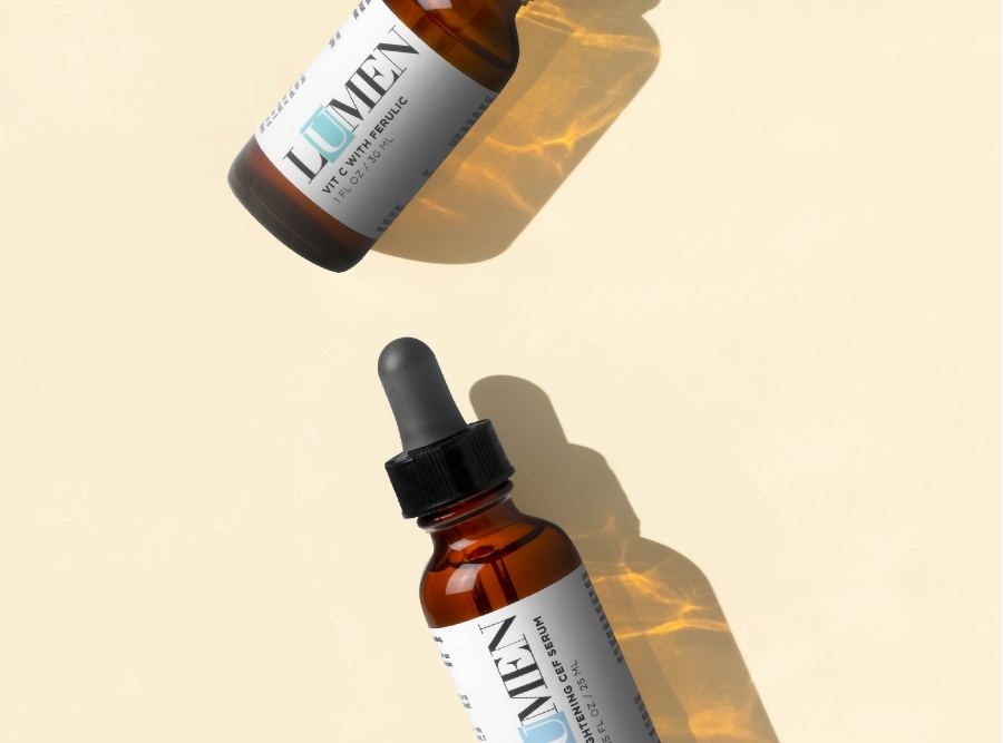 Lumen vitamin C serum with ferulic acid in amber glass dropper bottles on a light neutral background.